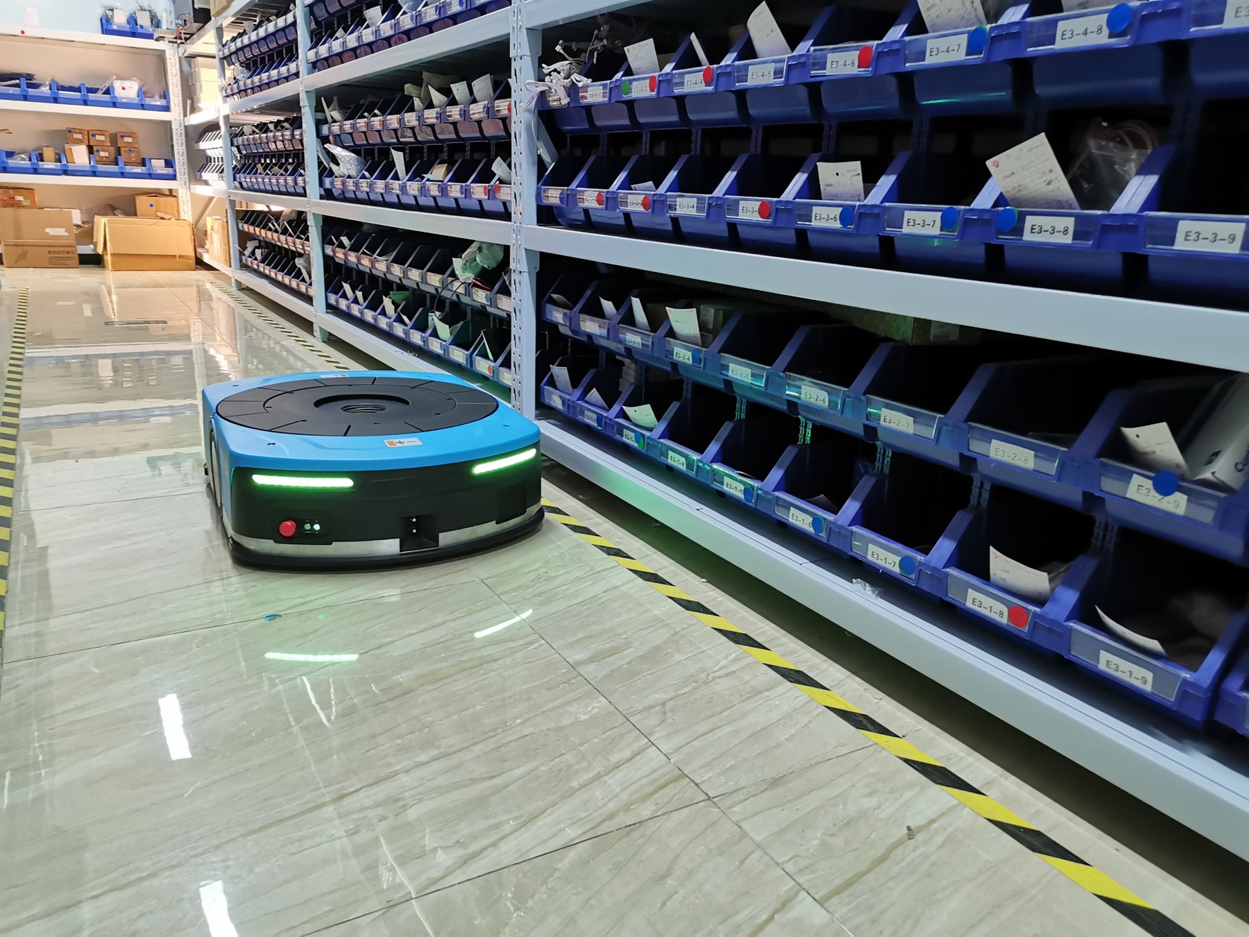 写真はAMB-800K(800kg可搬のSLAM式AMR)。ジャッキアップテーブルに回転機構を加えたことで、より安全に無駄のない搬送を実現。かご車、ピッキングカート、パレタイズ商品等を無人で積込み・搬送・積降しすることが可能。