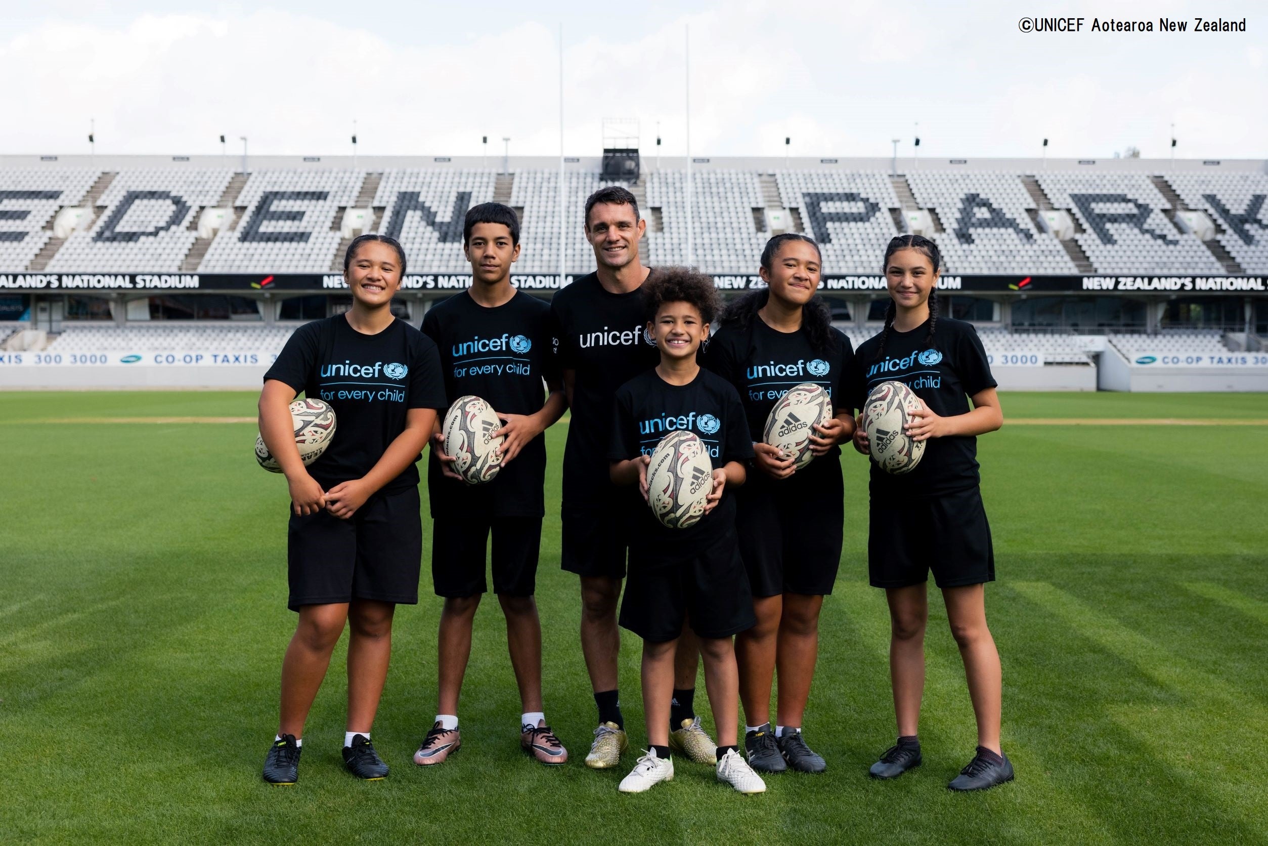 オークランドにあるニュージーランド最大のスタジアム、イーデンパークで子どもたちと並ぶカーター氏。DC10基金を立ち上げた、元オールブラックスのダン・カーター氏。© UNICEF Aotearoa New Zealand