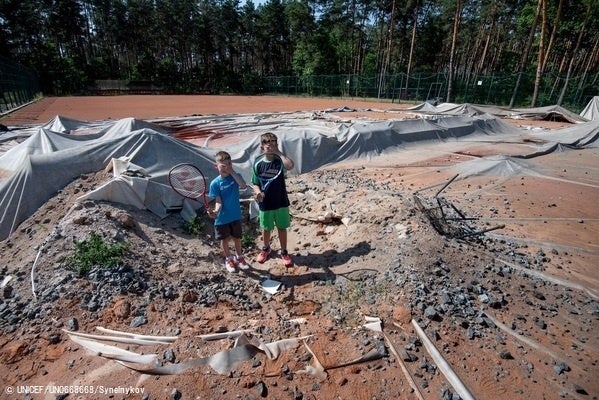 砲撃や爆撃を受けて破損したテニスコートに立つ子どもたち。このテニスコートで、テニスの大会が行われる予定だった。(ウクライナ、2022年6月撮影) © UNICEF_UN0668668_Synelnykov