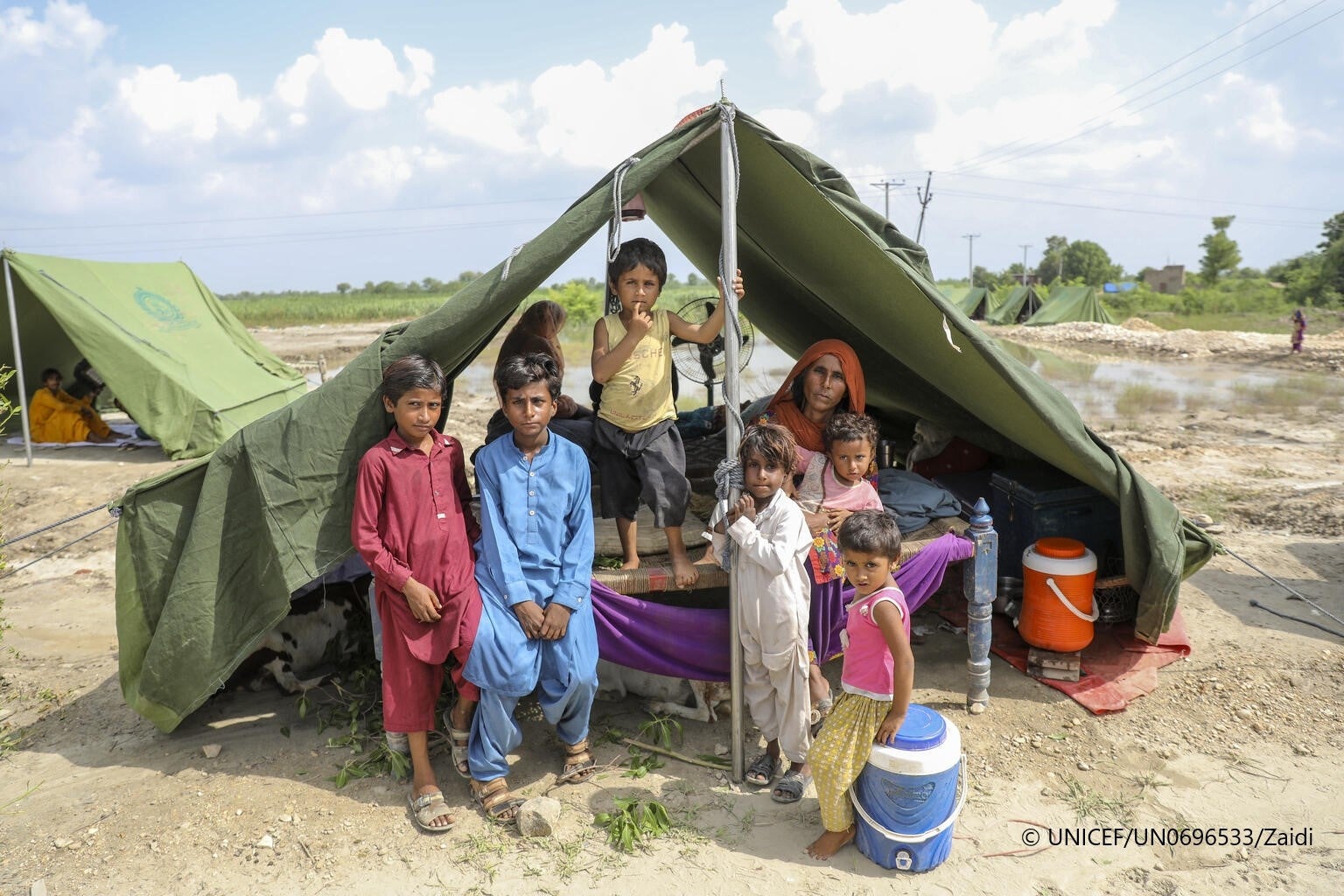 洪水の避難民のためのテントで一時的に暮らす家族。子ども9人を抱える一家は、洪水で自宅も家畜も失った。テントが見つかるまでの2週間、道路脇の野外で座り込んでいたという。（シンド州、2022年8月29日撮影）© UNICEF_UN0696533_Zaidi