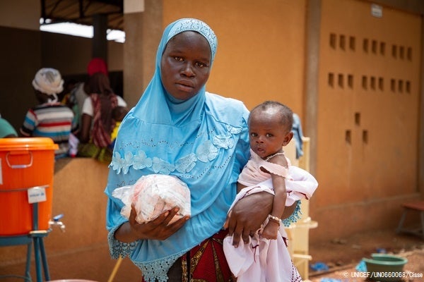 重度の急性栄養不良で生後6カ月のアブドゥルちゃんを抱く母親。カヤの保健センターで、子どもの栄養治療食のプランピーナッツを受け取った。(ブルキナファソ、2022年6月撮影) © UNICEF_UN0660068_Cisse