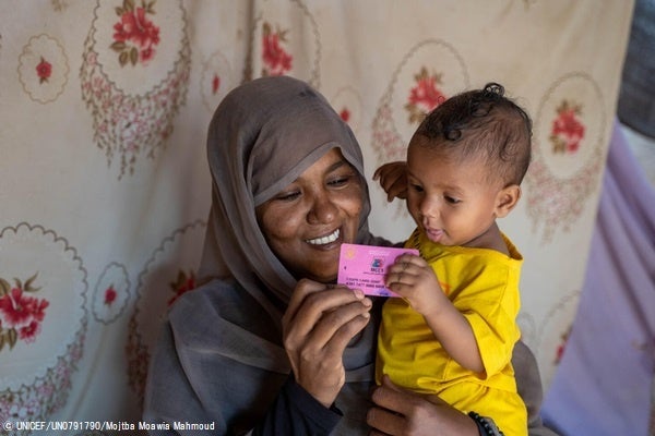 カッサラ州で、ユニセフが支援する母子現金給付プログラムの登録カードを受け取った生後9か月の娘を抱く母親。(スーダン、2023年2月22日撮影) © UNICEF_UN0791790_Mojtba Moawia Mahmoud