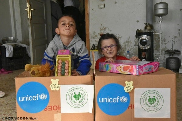 ハマにある避難所で、おもちゃや洋服のユニセフの支援物資を受け取る5歳のアブルドゥルハディちゃんとシャムちゃん。(シリア、2023年3月撮影) © UNICEF_UN0804964_Hazori