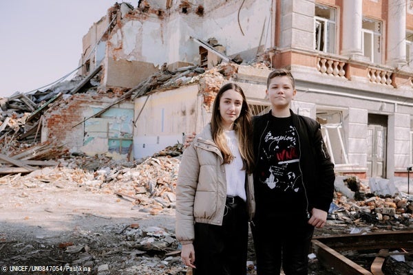 ハルキウ州で紛争の被害を受け、破壊された学校の前に立つ17歳のアナスタシアさんと12歳のミハイロさん姉弟。(ウクライナ、2023年4月撮影) © UNICEF_UN0847054_Pashkina