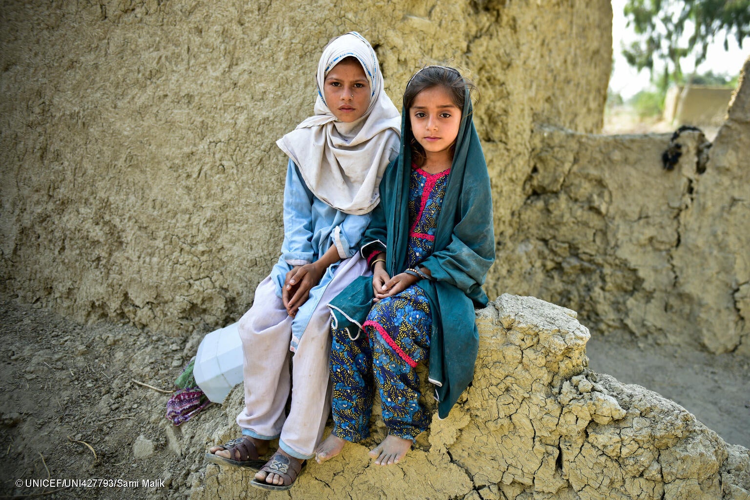 泥で作られた自宅が洪水被害に遭い、壊れた壁に座る7歳のムリコさんと6歳のテシーンさん姉妹。 (パキスタン、2023年8月24日撮影) © UNICEF_UNI427793_Sami Malik