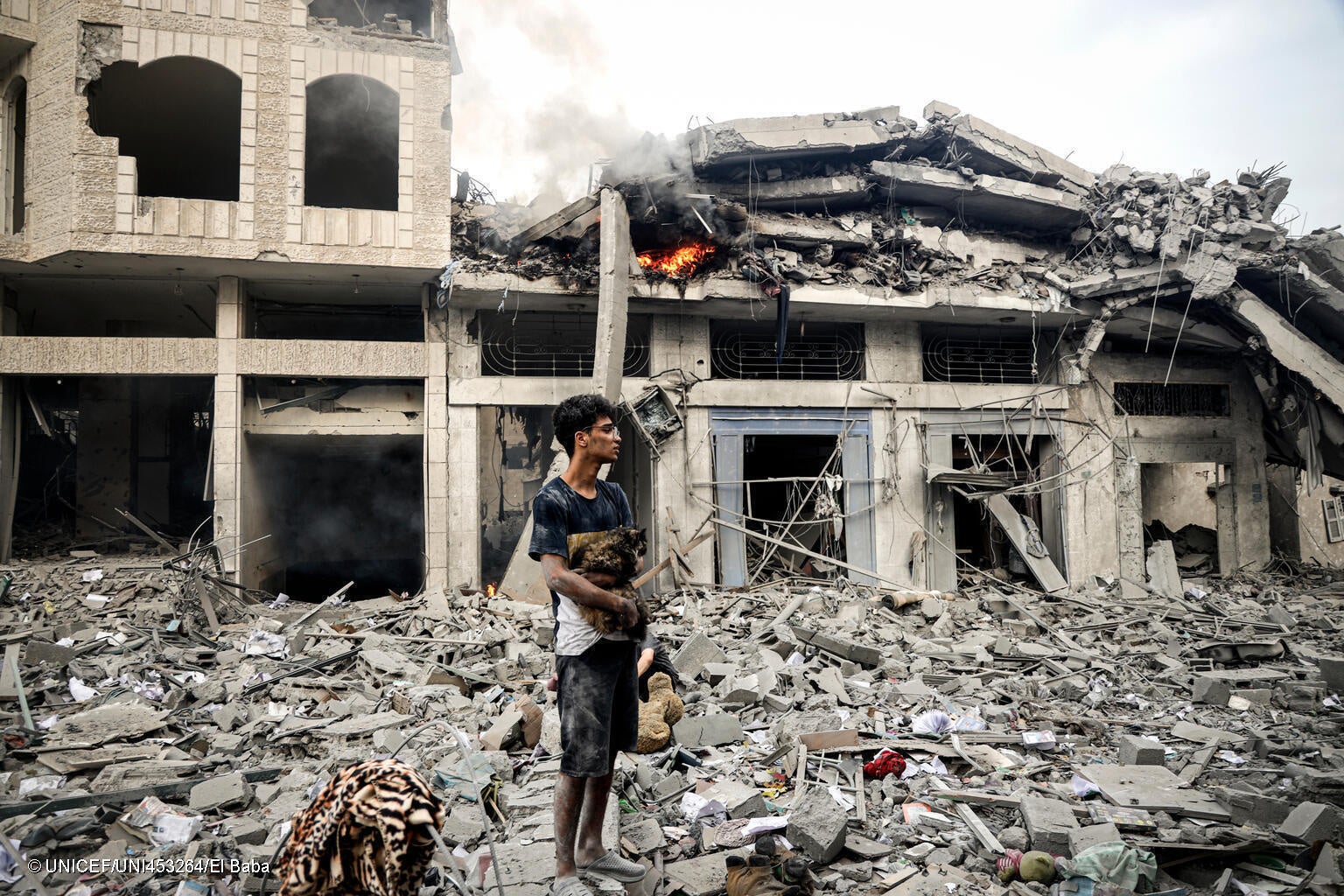 ガザ地区で、爆撃により倒壊した建物の瓦礫の上で、飼っている猫を抱きながら立ち尽くす15歳のカリムさん。(ガザ地区、2023年10月14日撮影) © UNICEF_UNI453264_El Baba