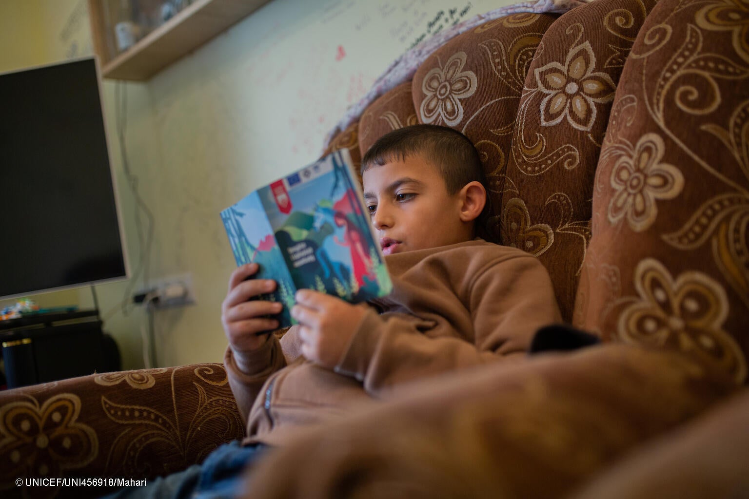 祖母と3人の兄弟たちと避難し、仮住まいしている家で本を読む8歳のアルメンさん。避難途中で父親が爆発に巻き込まれ亡くなってしまった。(アルメニア、2023年10月13日撮影) © UNICEF_UNI456918_Mahari