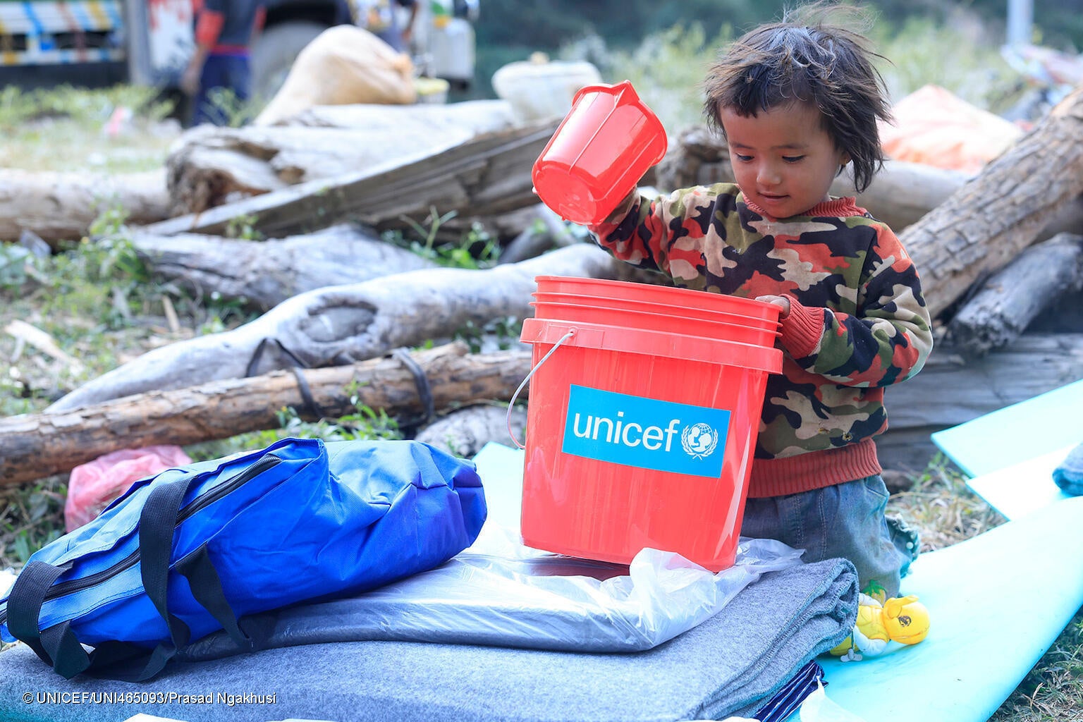 地震の被害が最も甚大だった地域のひとつ、ルクム西部のAathbiskotに届けられた、防水シートや毛布、衛生キットなどを含むユニセフの支援物資を受け取った子ども。(ネパール、2023年11月6日撮影) © UNICEF_UNI465093_Prasad N