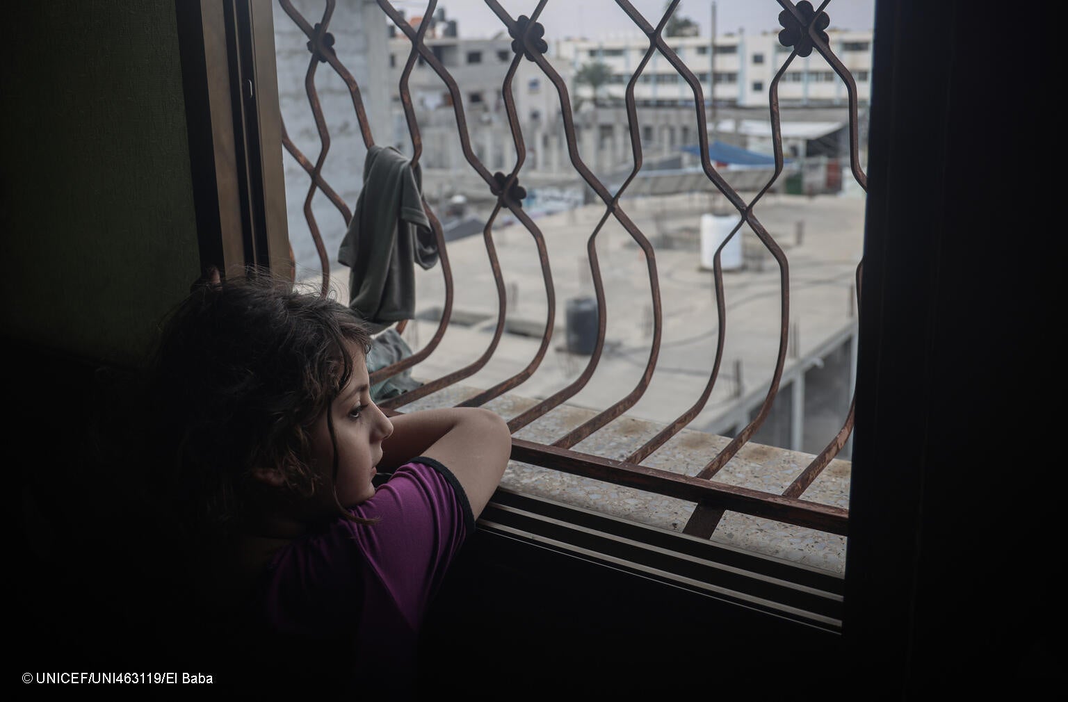 部屋の窓から外を見る女の子。(ガザ地区、2023年11月2日撮影) © UNICEF_UNI463119_El Baba