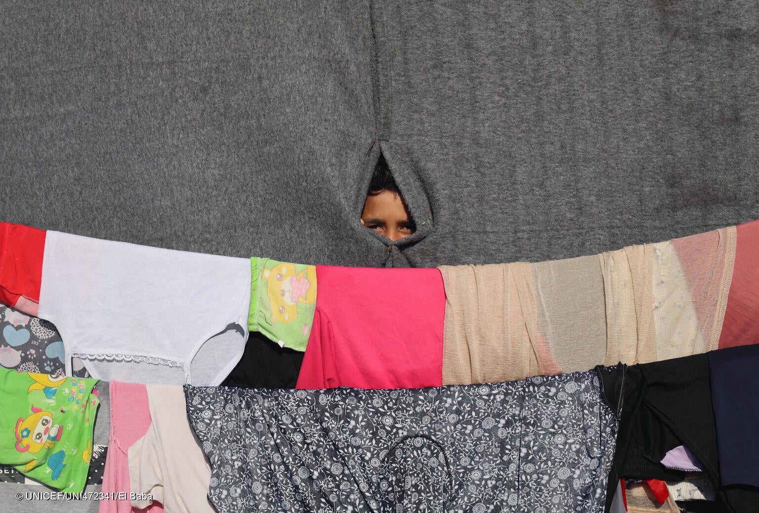 ハンユニス避難民キャンプのテントの中から、外を眺める子ども。(ガザ地区、2023年11月15日撮影) © UNICEF_UNI472341_El Baba