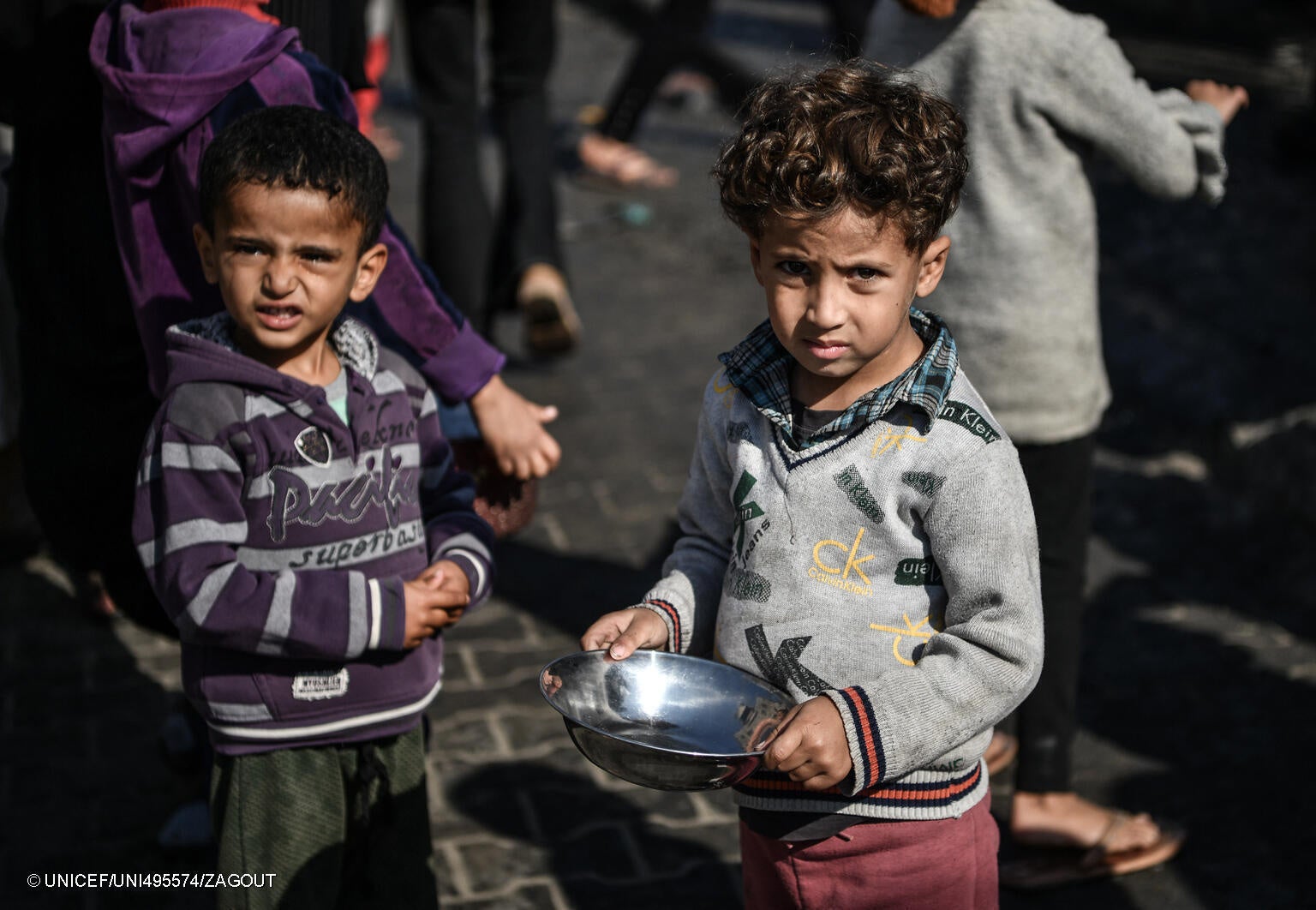 炊き出しを受け取るための順番待ちをする兄弟。「お腹が空いている。ご飯を受け取りたくて、ここでずっと待っているんだ」と話す。(ガザ地区、2023年12月19日撮影) © UNICEF_UNI495574_ZAGOUT