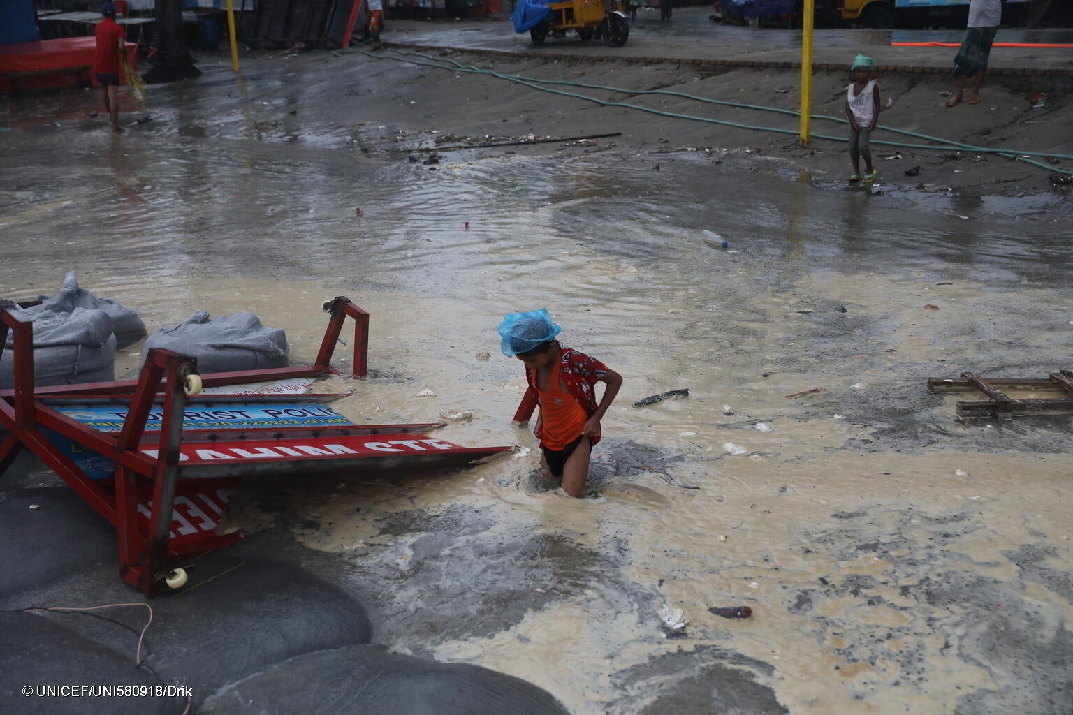 サイクロンで水没した道を渡る子ども。ユニセフはサイクロン到来以前から、命を守る支援物資をすぐに届けられるよう準備をしており、被害が大きい地域に素早くスタッフを派遣できるよう待機させていた。(バングラデシュ、2024年5月26日撮影) © UNICEF_UN