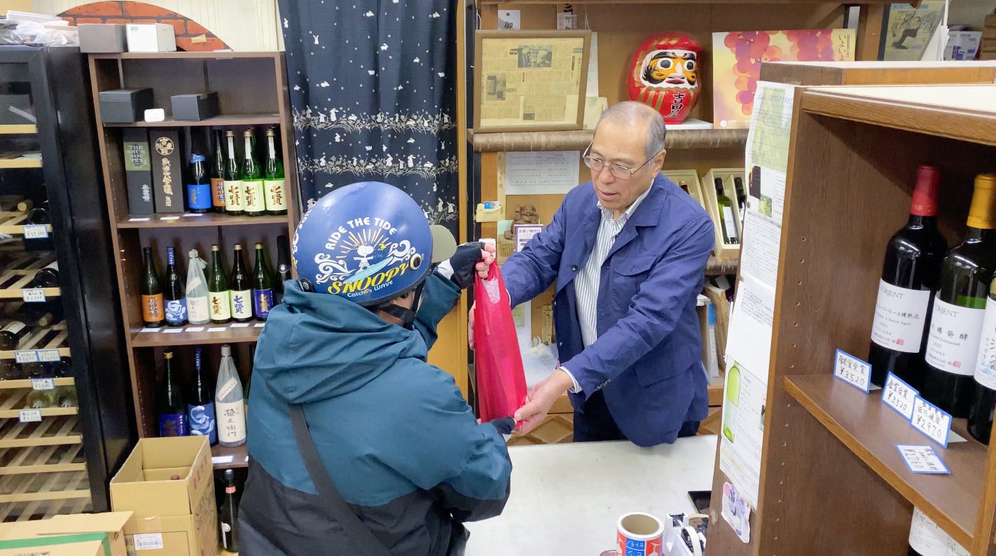 <注文の入った酒店でお買い物代行をする配達パートナーと店主>
