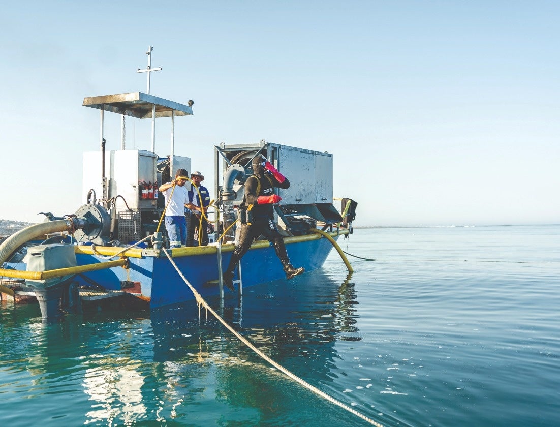 小さな船で出航し、ホースを持ったダイバーが海底へ潜る様子。