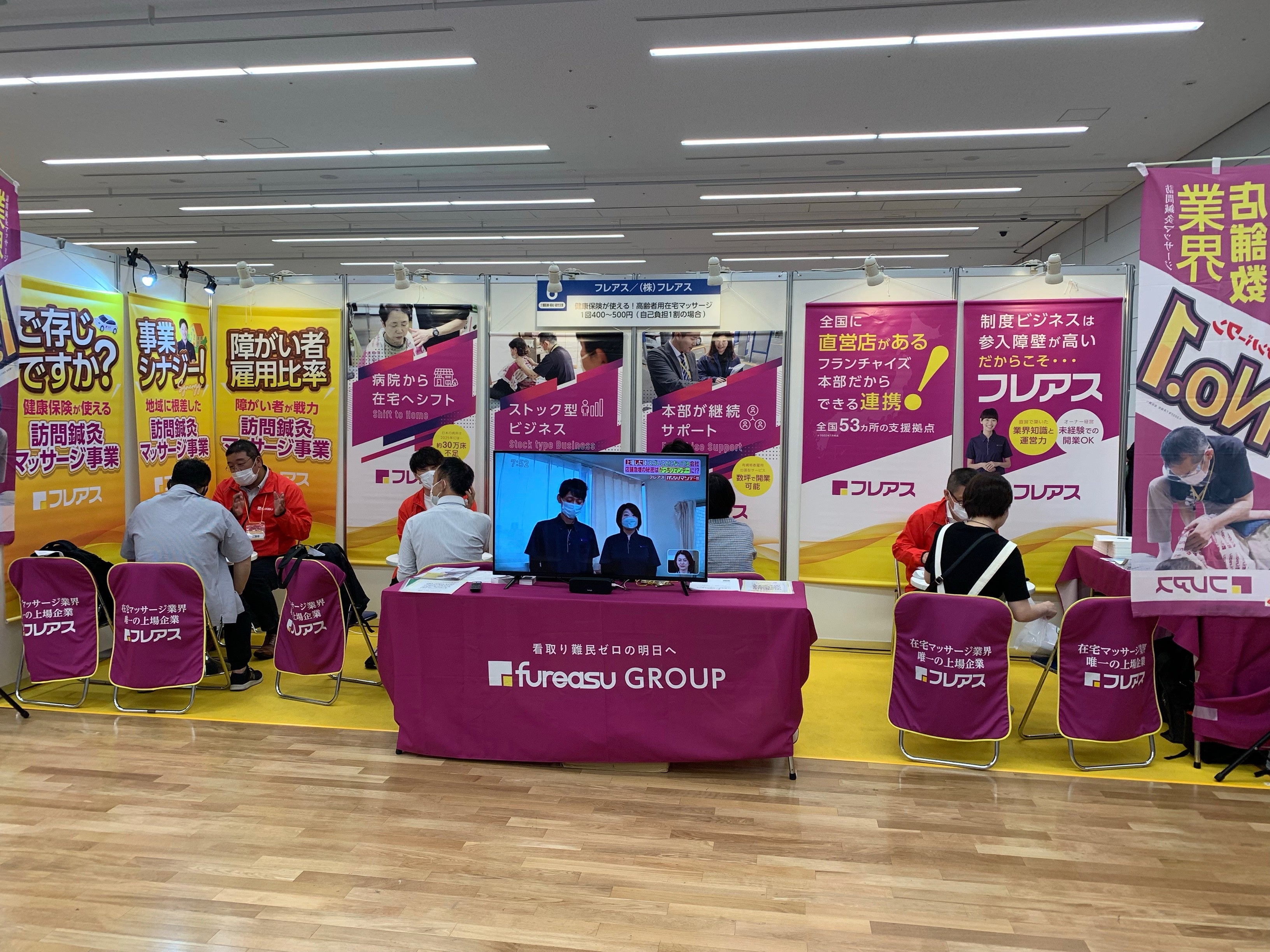 在宅マッサージ、訪問マッサージ事業を紹介する出展企業（株式会社フレアス）と来場者