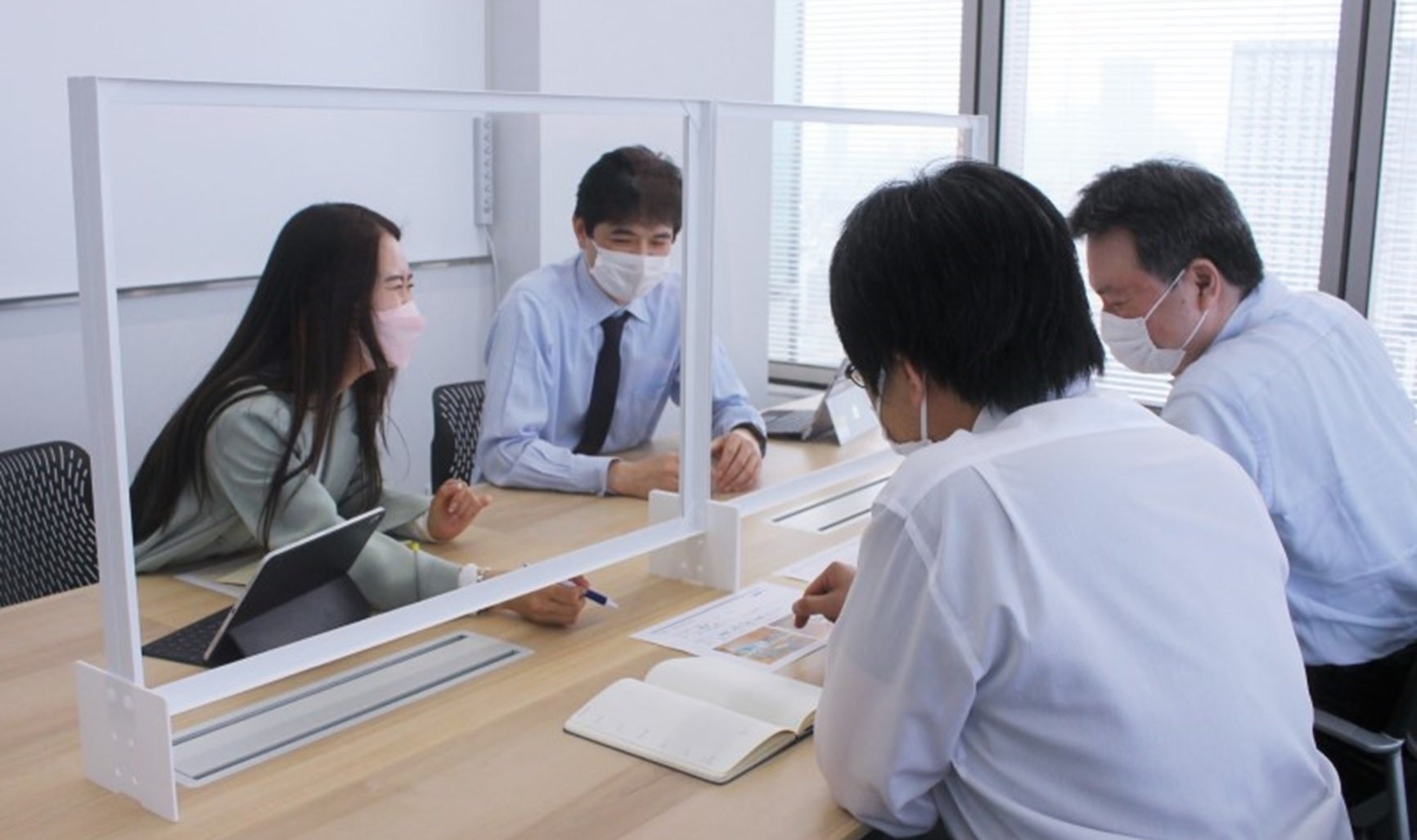 新型コロナウイルス等の感染防止対策として社内に導入した「DNP低反射・低遮音フィルムパーティション」を使って議論する様子 