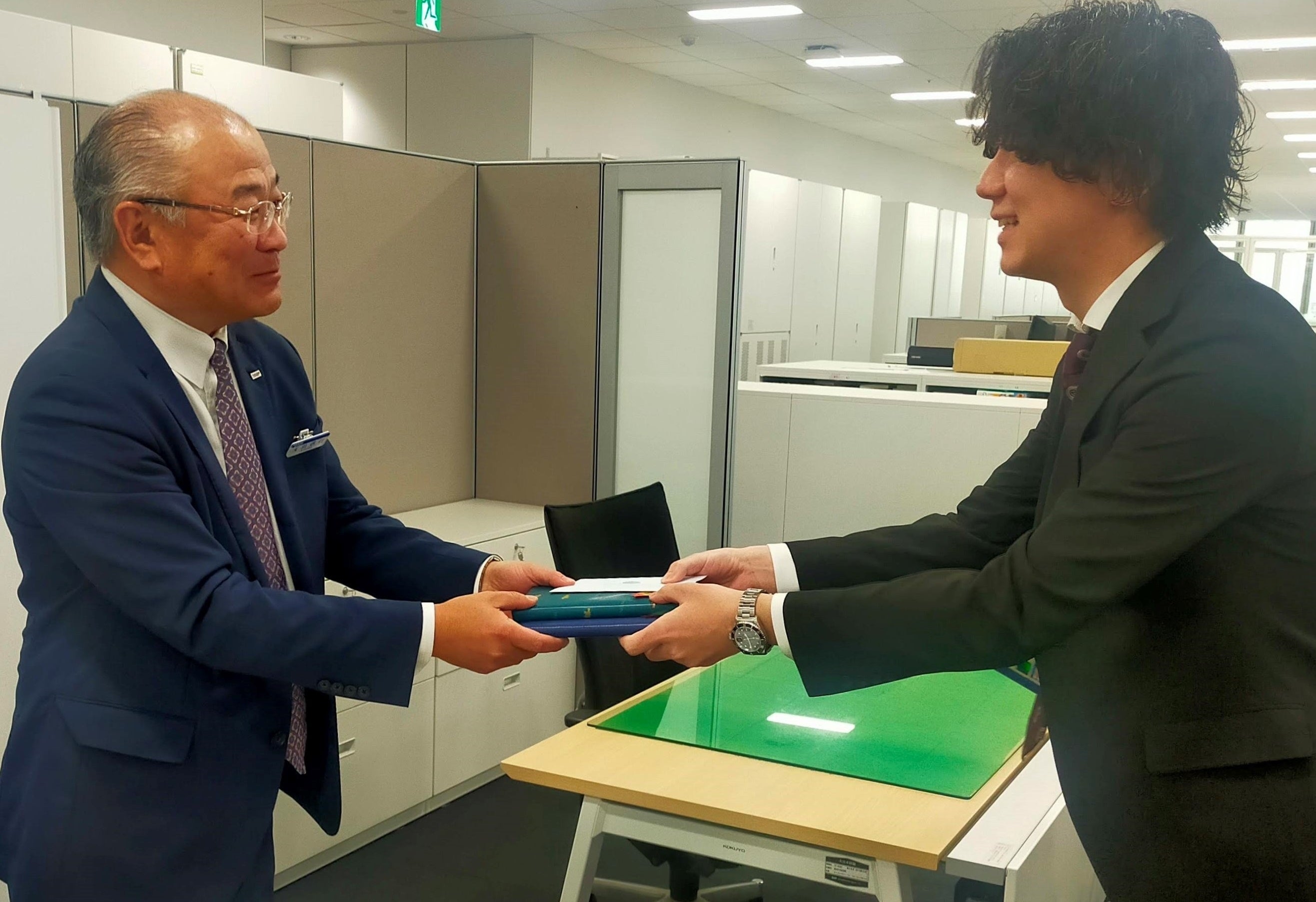 若手社員（右）が事業部長（左）に本を贈る様子