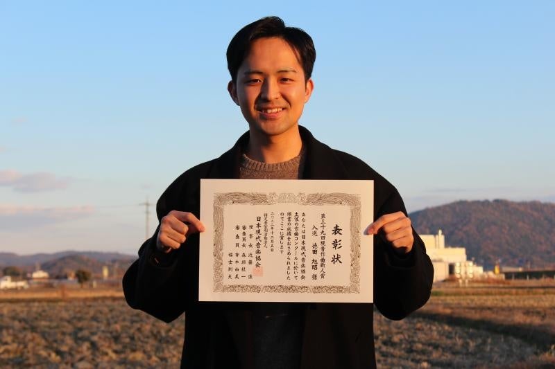 「Roots by Arcangelo Corelli」を作曲するなかで、インスピレーションを得たという総社市の田園で表彰状を手にする徳田さん
