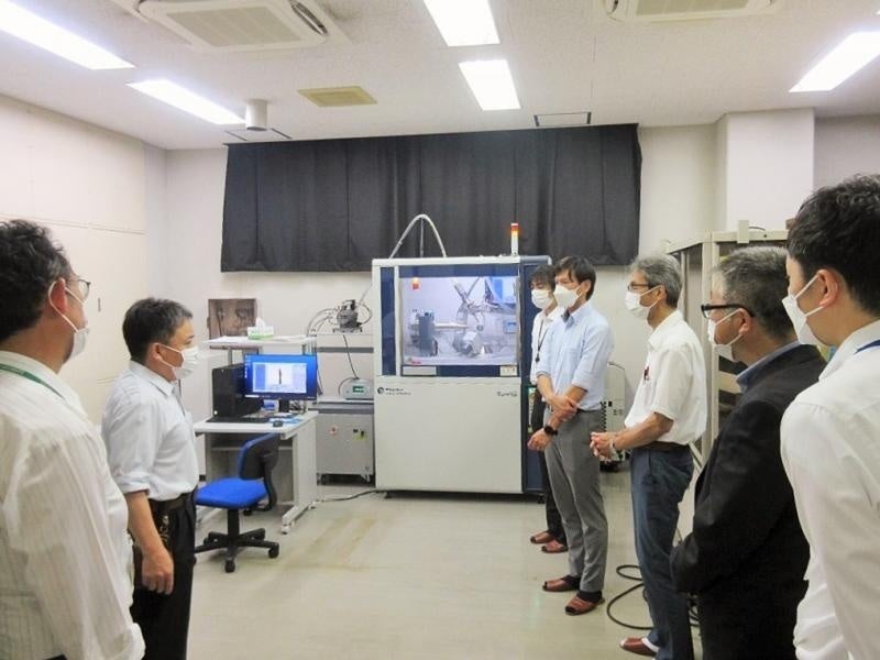 機器分析実験施設の担当技術職員から機器共用について説明を受ける本学訪問者ら（右）