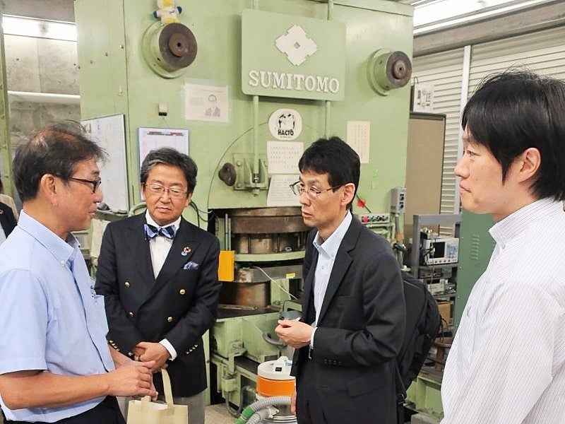 超高圧発生装置と研究試料を基に高温・高圧実験について紹介する芳野所長（左）、後ろは一軸加圧式川井型超高圧発生装置（USSA-5000）