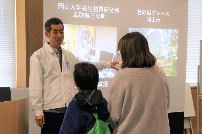 来場した小学生に電子顕微鏡を用いた小惑星リュウグウ試料の観察について説明をする田中亮吏教授