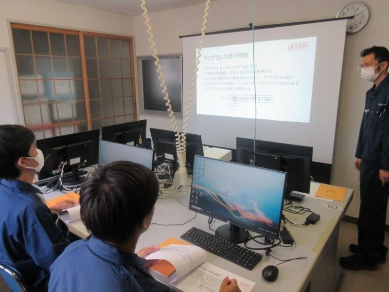 尾﨑技術専門職員(奥)からプログラムの説明を受けるTR(手前)