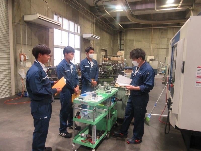 藤本技術職員(右)から工作機械の説明を受けるTR(左)
