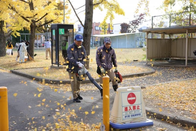 作業員とともにブロワーで落ち葉を飛ばす那須学長(左)