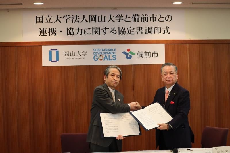 協定書を手に固く握手を交わす吉村武司市長（右）と槇野博史学長　※撮影時のみマスクを外しました