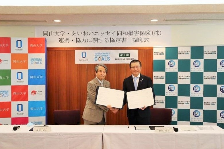 協定書を手に固く握手を交わす新納社長(右)と槇野学長