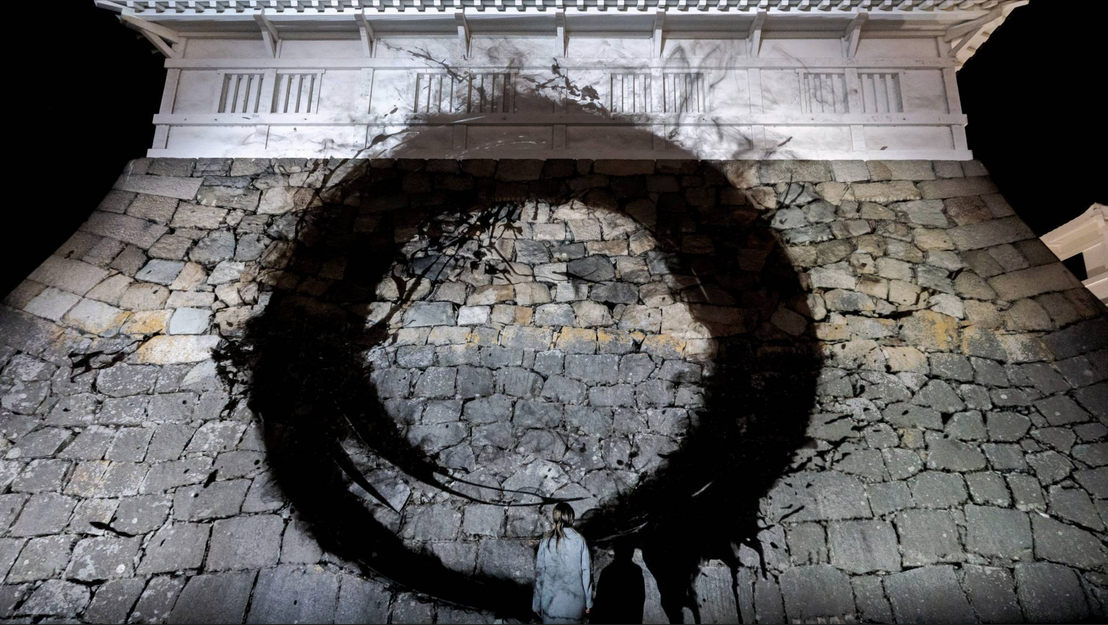 光で描かれる書の黒は、光がないことを意味し、数百年の長い時間による風化が生んだ石垣がつくる影と区別がつかない。チームラボ《古えの石垣の円相》© チームラボ