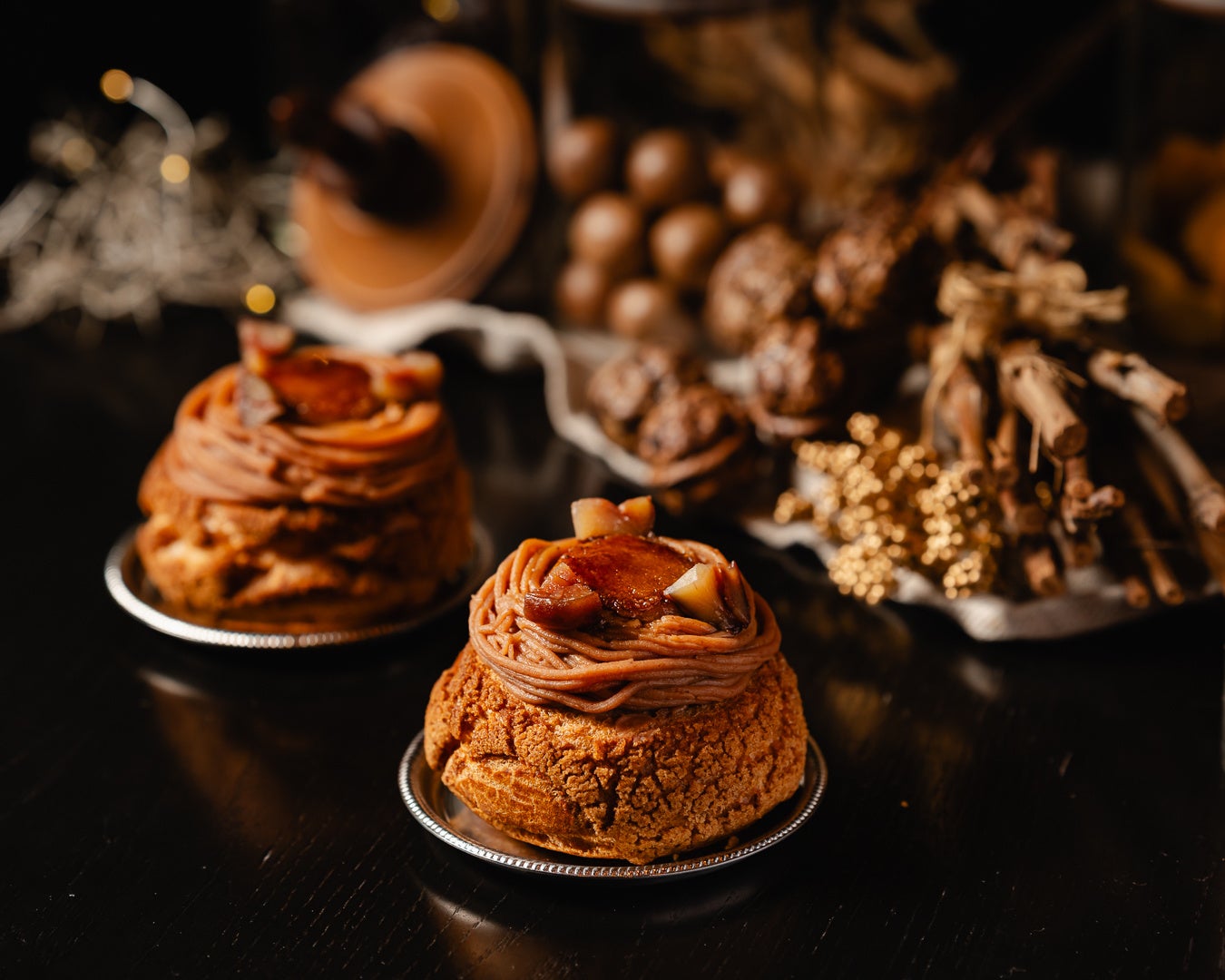 モンブランクリームと渋皮煮をのせ、表面を香ばしくブリュレしたシュー。秋色の小物を背景に2個並ぶ商品写真（MAISON CLASSIC）