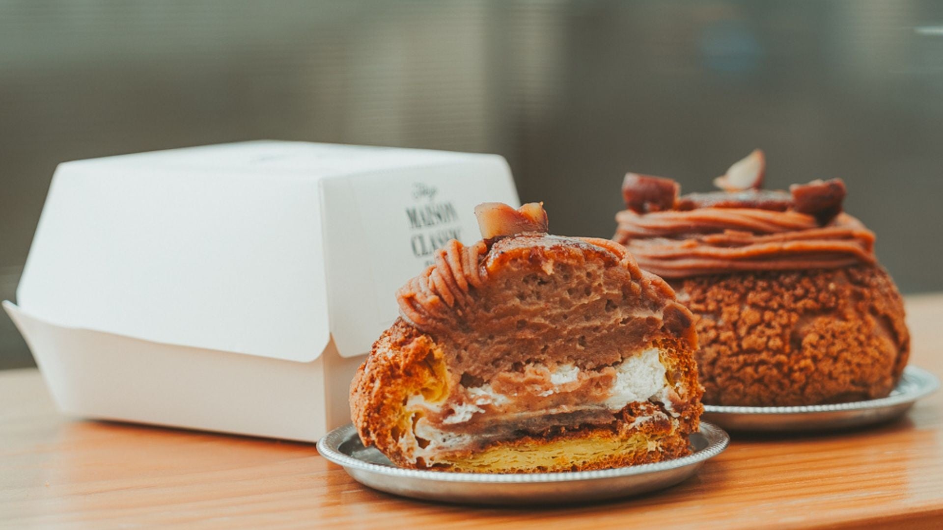 シューを半分にカットした断面。カスタード・クリーム・モンブラン層が見える。奥にホールの同商品と白い箱（MAISON CLASSIC）