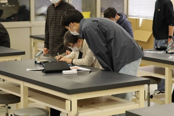 ハンダ付けのサポートをする学生