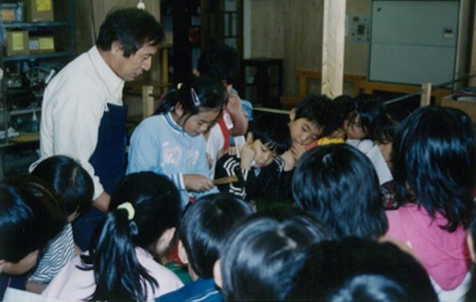 工房での社会科見学の様子(2000 年頃)。子どもたちに囲まれて話す様子