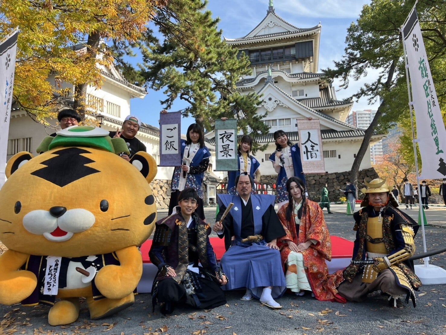 上段左から、MCのメガモッツ、直筆の掛け軸を持った金子有希さん、前田佳織里さん、高田憂希さん 下段左から、小倉城マスコットキャラクター「とらっちゃ」、小倉城武将隊のみなさん