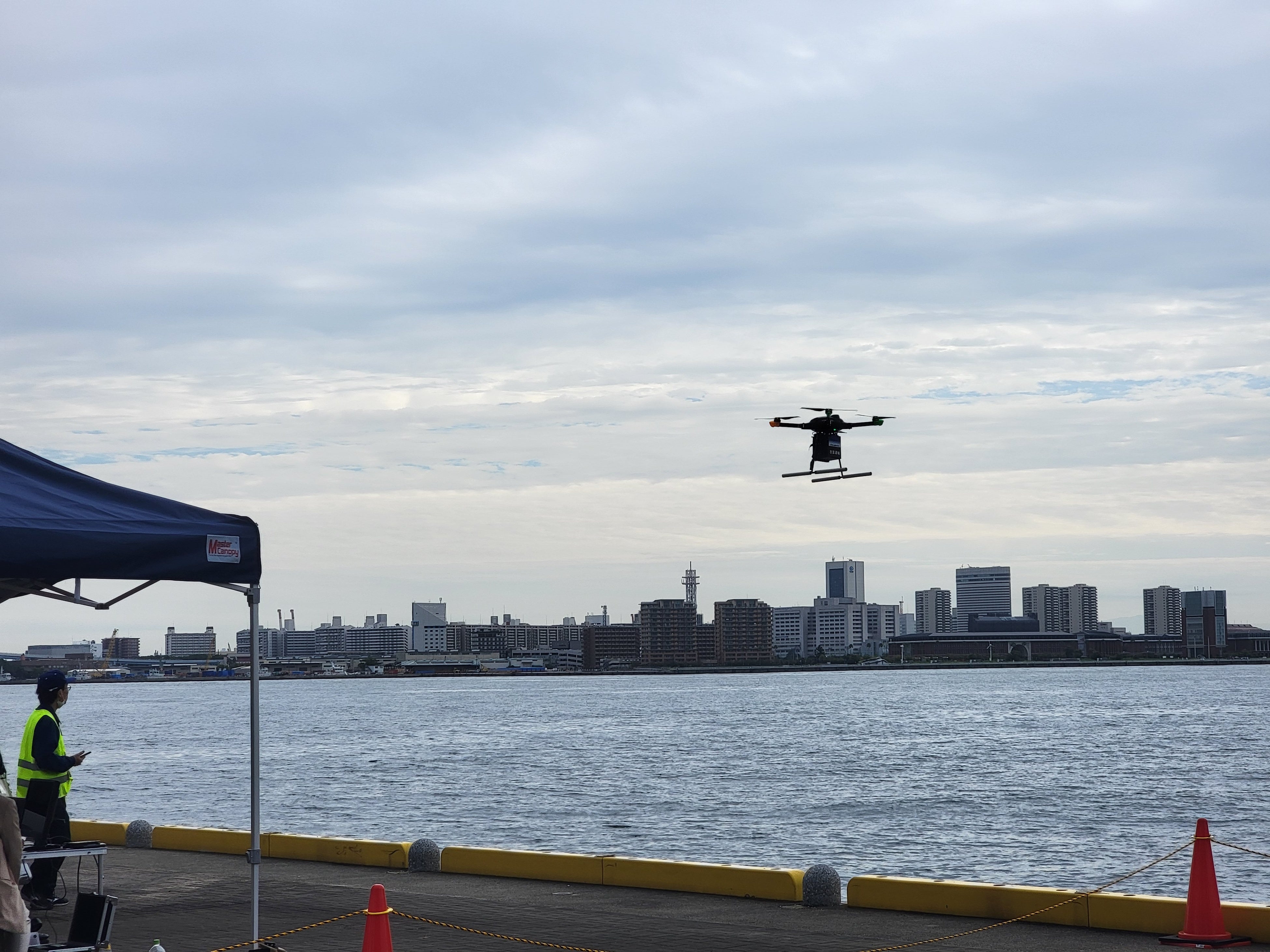 商品が入ったドローンが神戸港をわたってポートアイランドへ