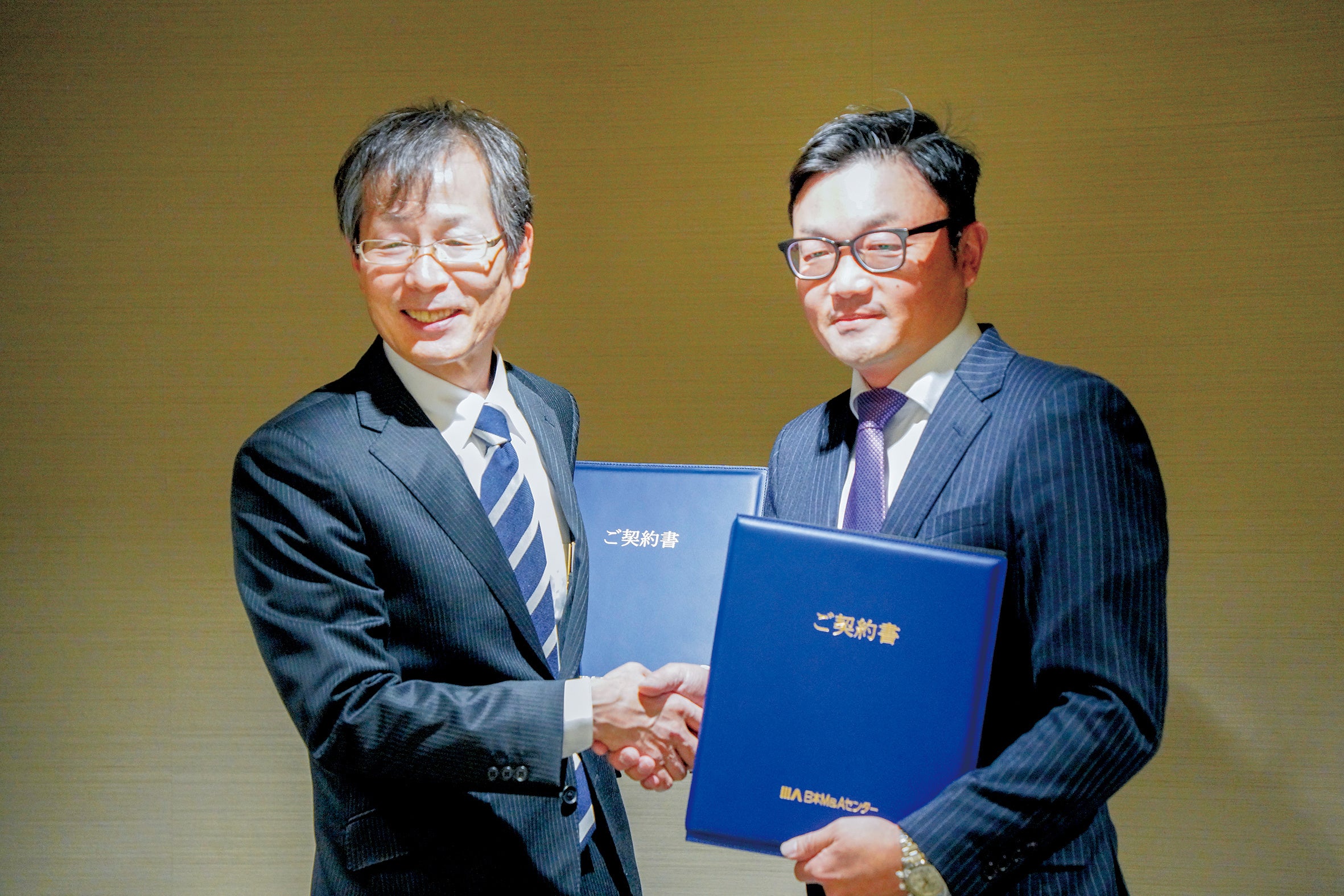 2022年12月12日に甲府市内のホテルで行われた成約式。固い握手を交わす石原敬三氏（左）と林正太郎氏（右）
