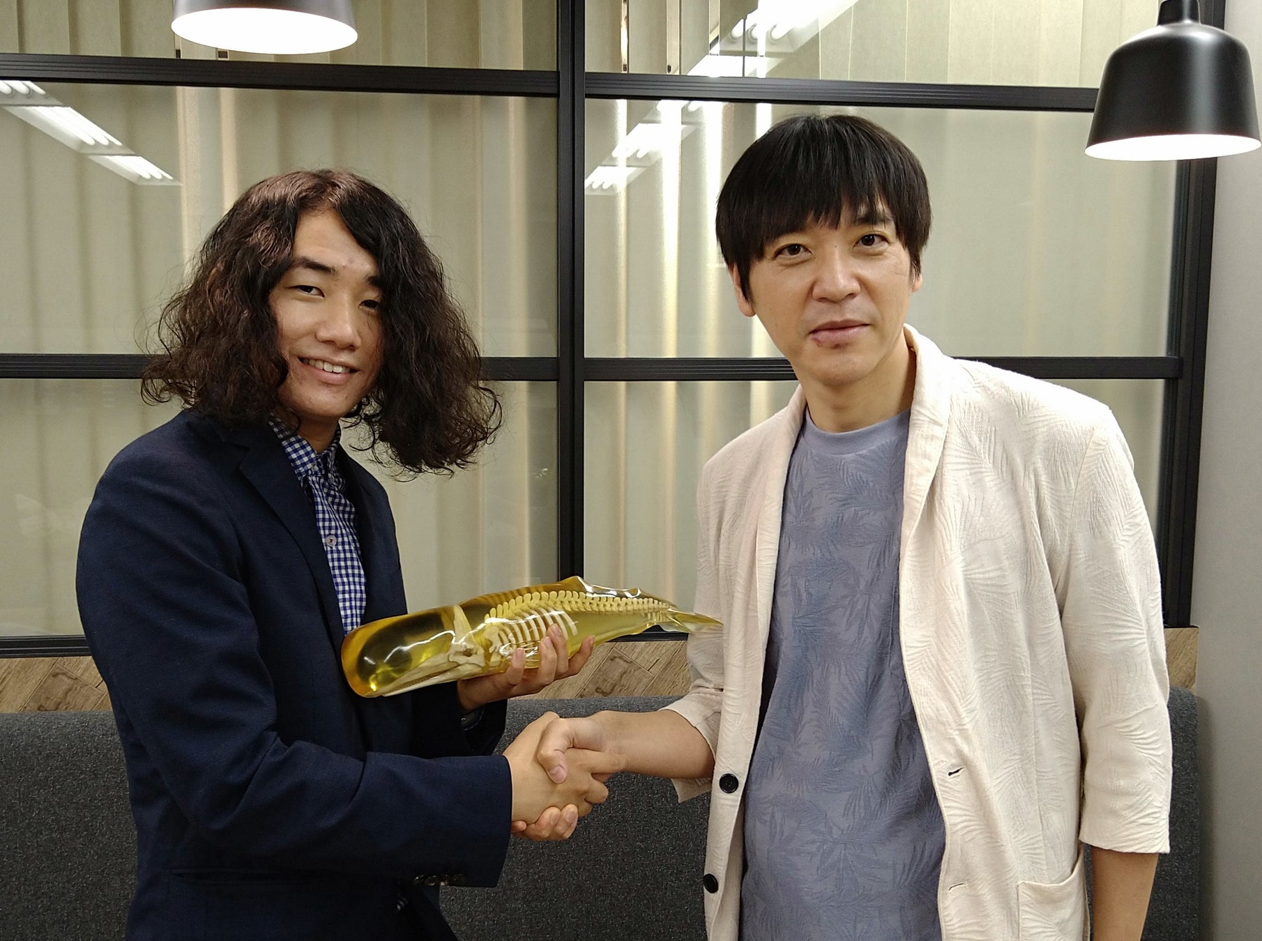 業務提携で合意し握手する株式会社ワールドエッグス代表取締役社長 波房克典(右)と                     合同会社吉本アートファクトリー代表 吉本大輝 氏