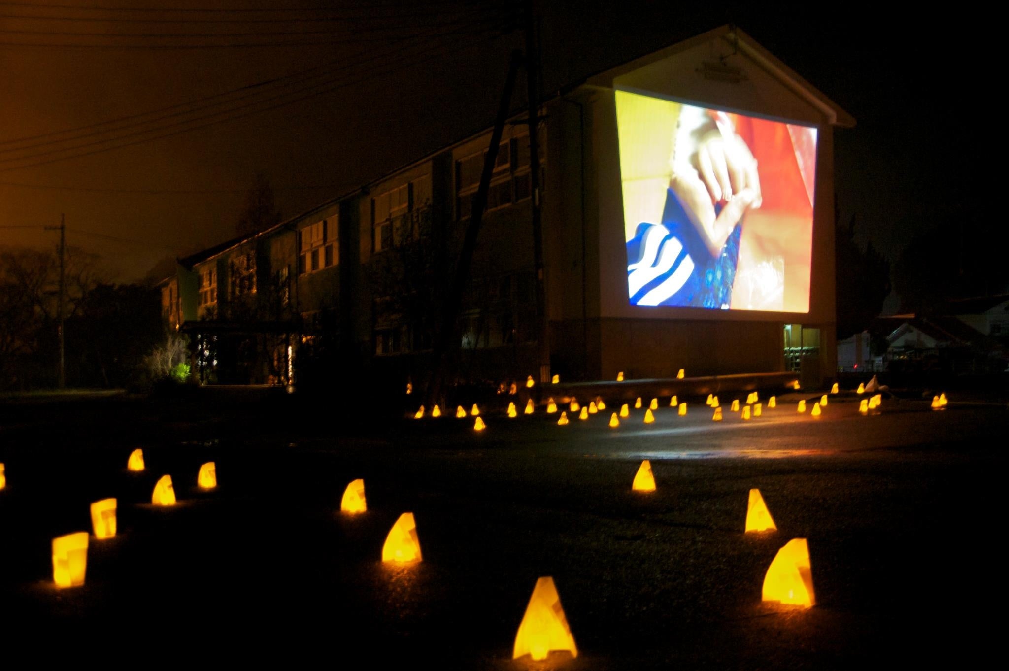 廃校の壁面に、映像作品を投影。周囲には、地域の方々が制作した灯ろうを設置。