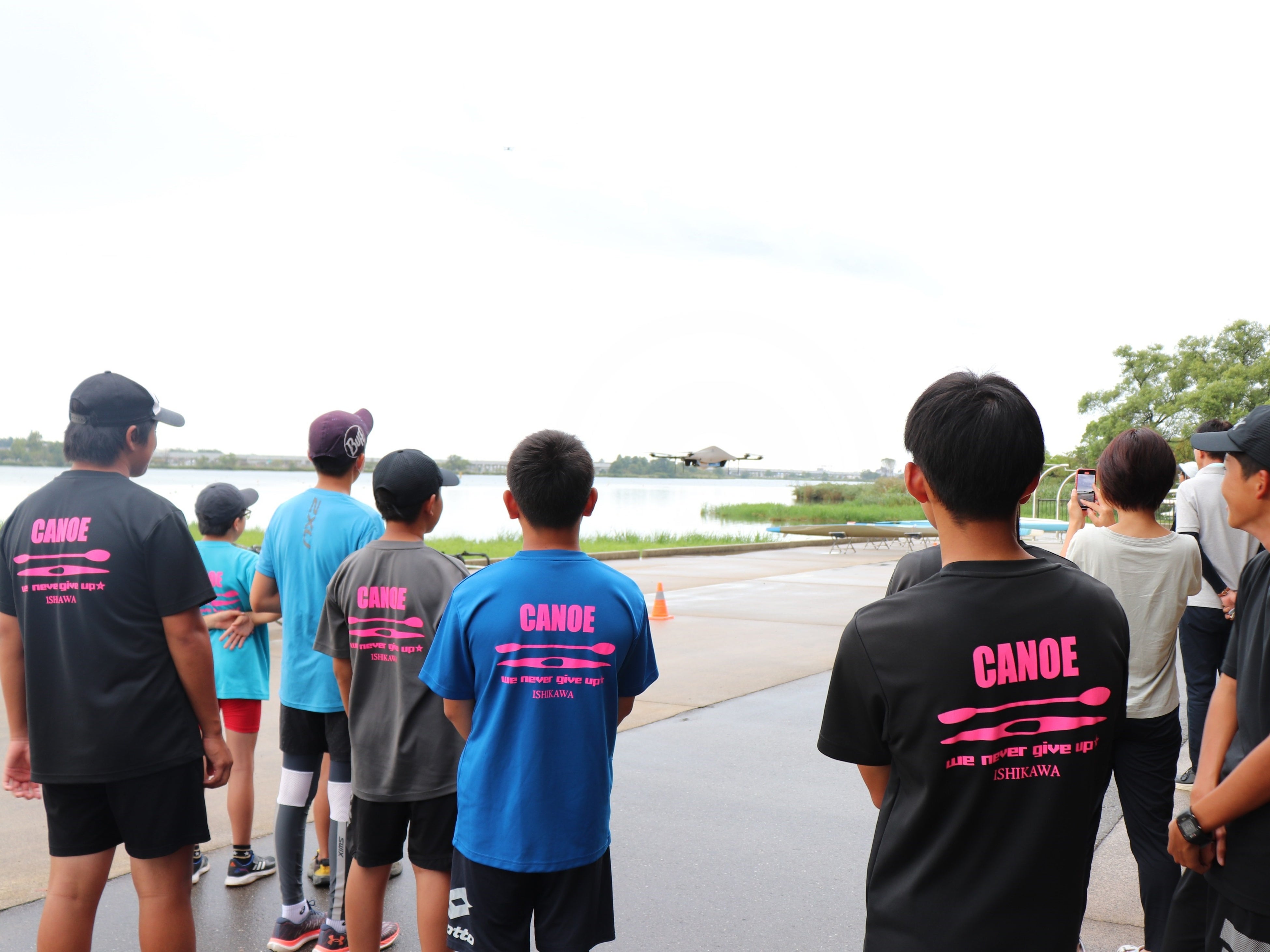 牛丼弁当がドローンで届く様子を見守る小松ジュニアカヌークラブの皆さん （木場潟カヌー競技場艇庫）