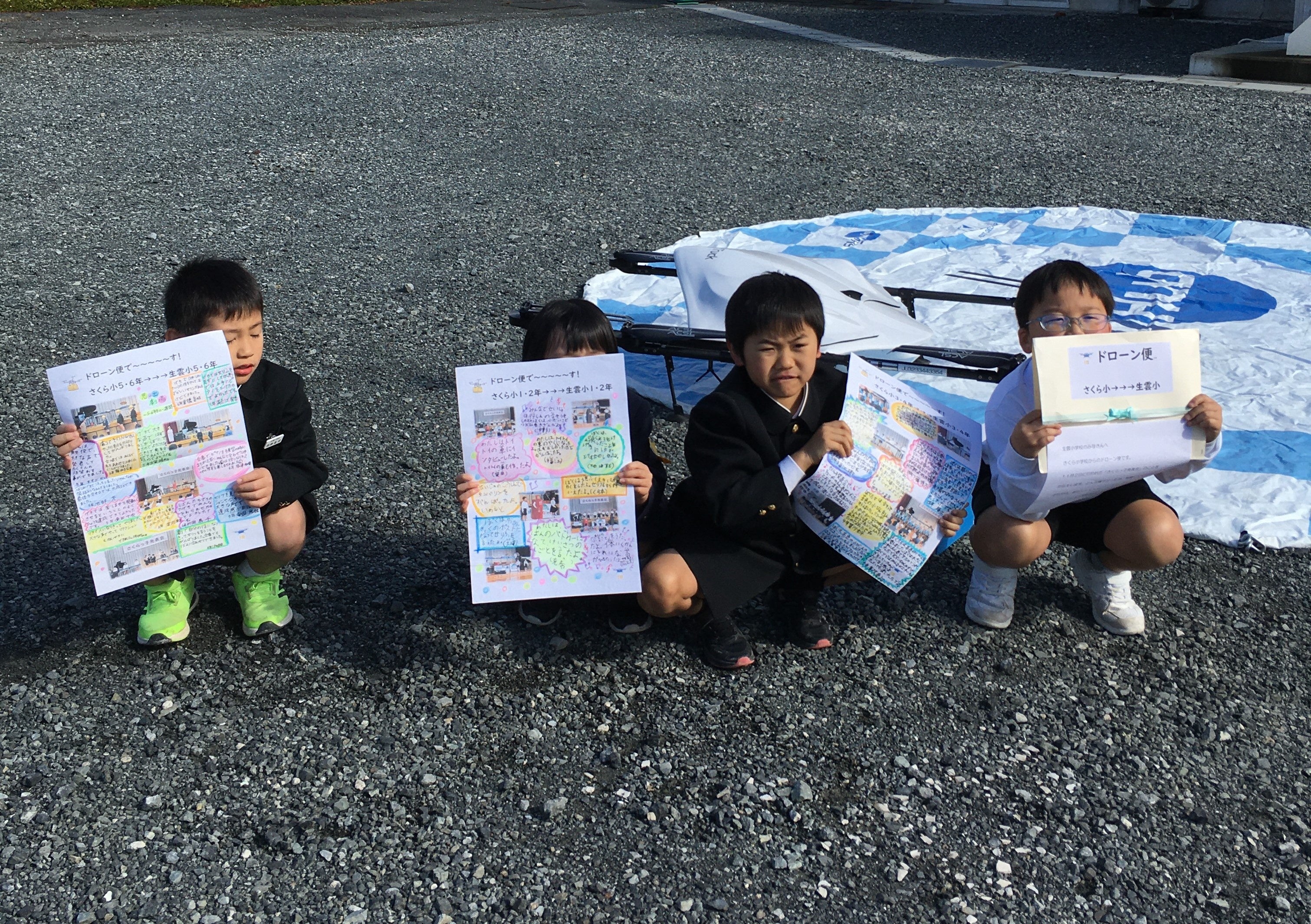さくら小学校の児童から送られた寄書を受け取った生雲小学校の児童と物流専用ドローン“AirTruck” （JAふれあい生雲支所駐車場）