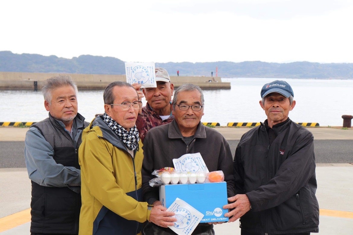 日本発物流専用ドローン“AirTruck”で配送された食料品を受け取ったみなさんと記念撮影（黒島港）