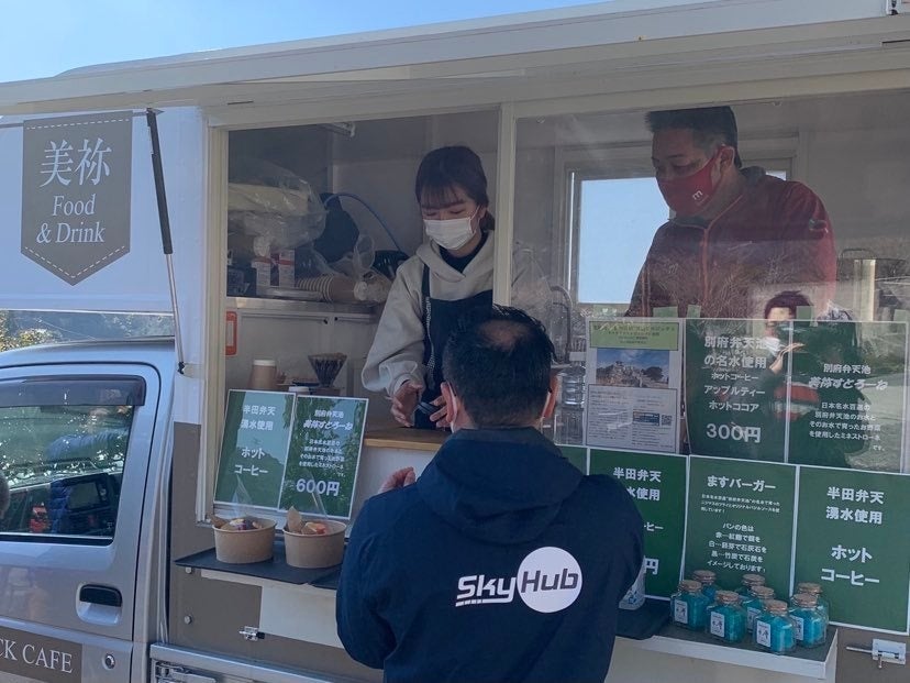 ドローンで届いた名水で淹れたコーヒーをキッチンカーから預かるSkyHub🄬スタッフ（秋芳八代ぬくもりの里）