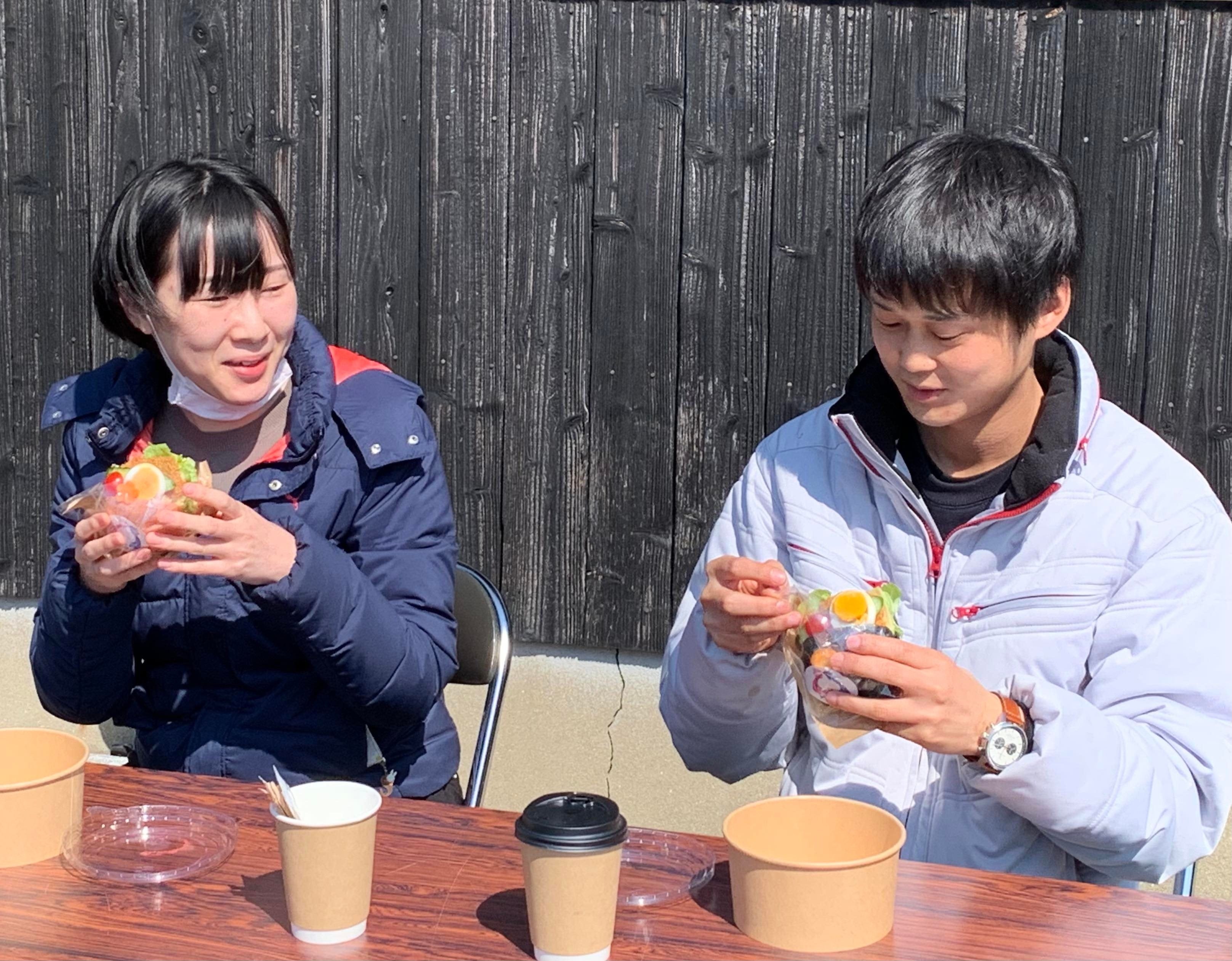 ドローン配送された名水で淹れたコーヒー とますバーガーを受け取って笑顔で食す 住民（栢木公会堂前）