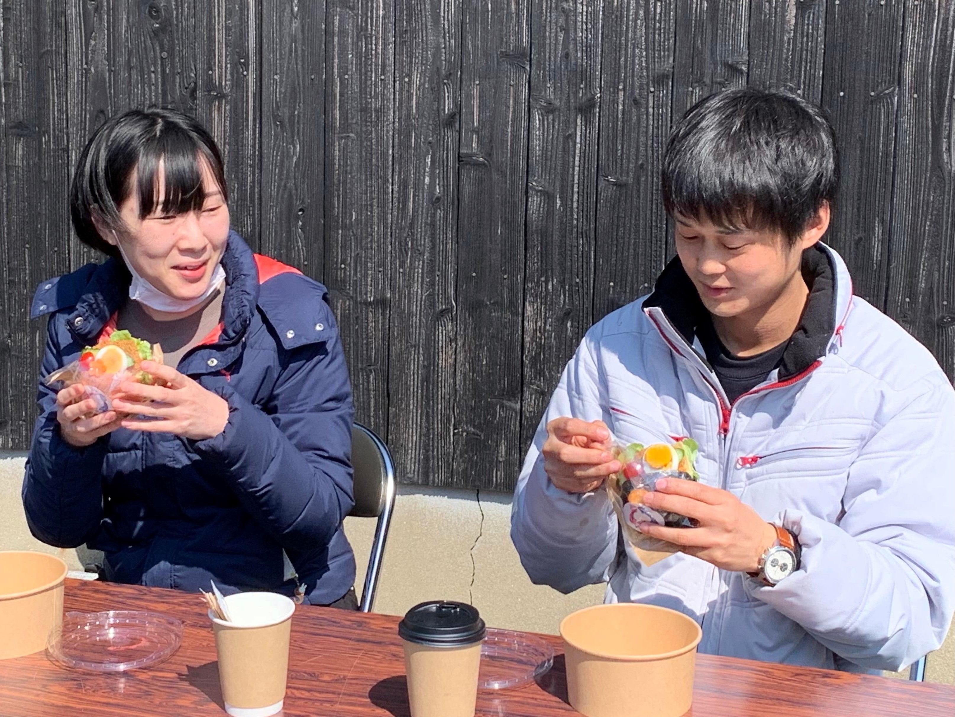 ドローン配送された名水で淹れたコーヒー とますバーガーを受け取って笑顔で食す 住民（栢木公会堂前）