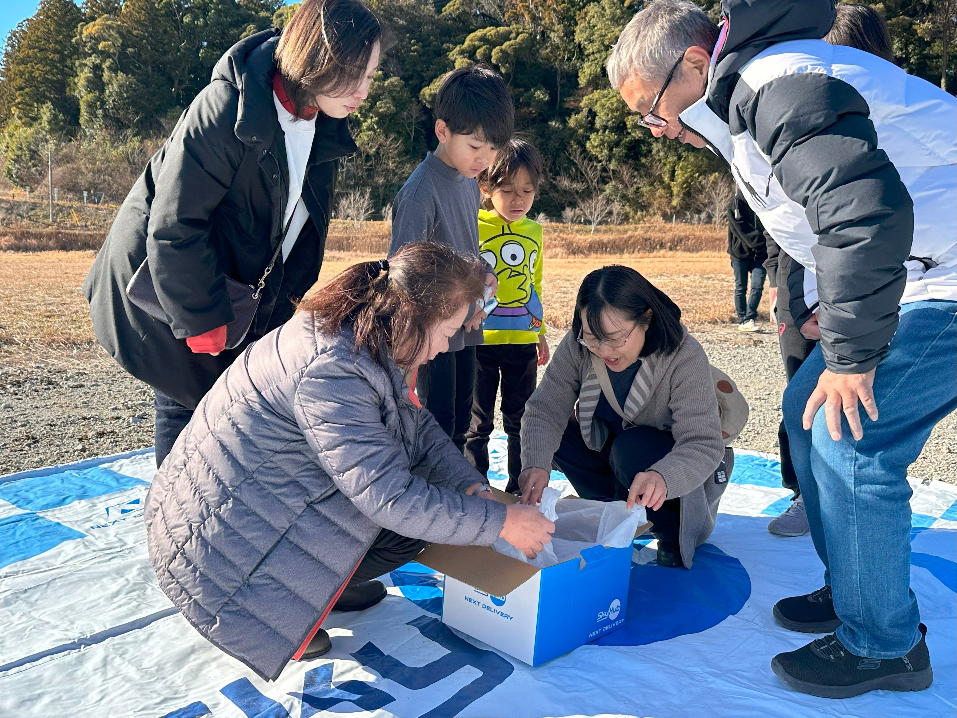 ドローンで配送されたものを確認する住民たち