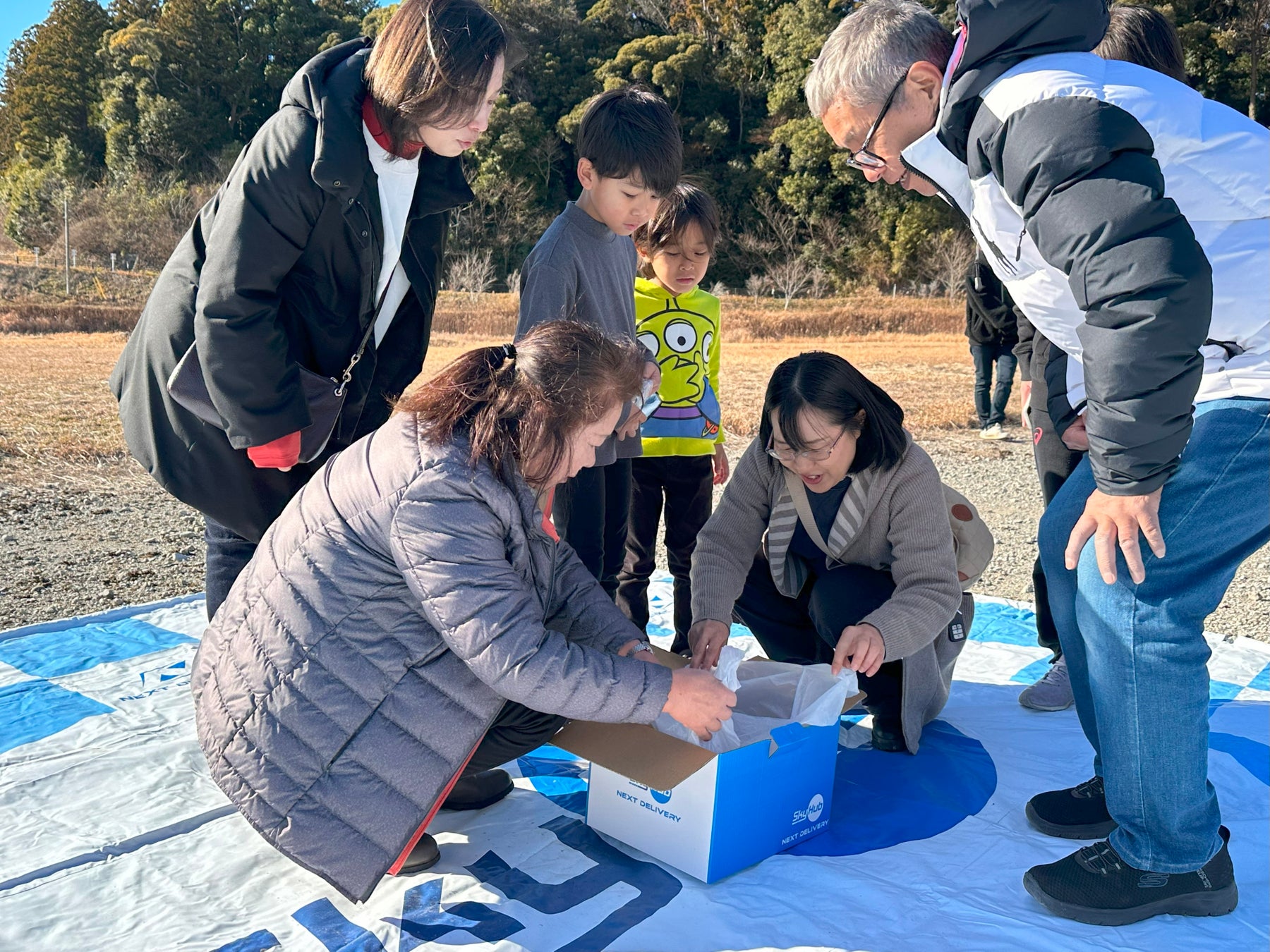 ドローンで配送されたものを確認する住民たち