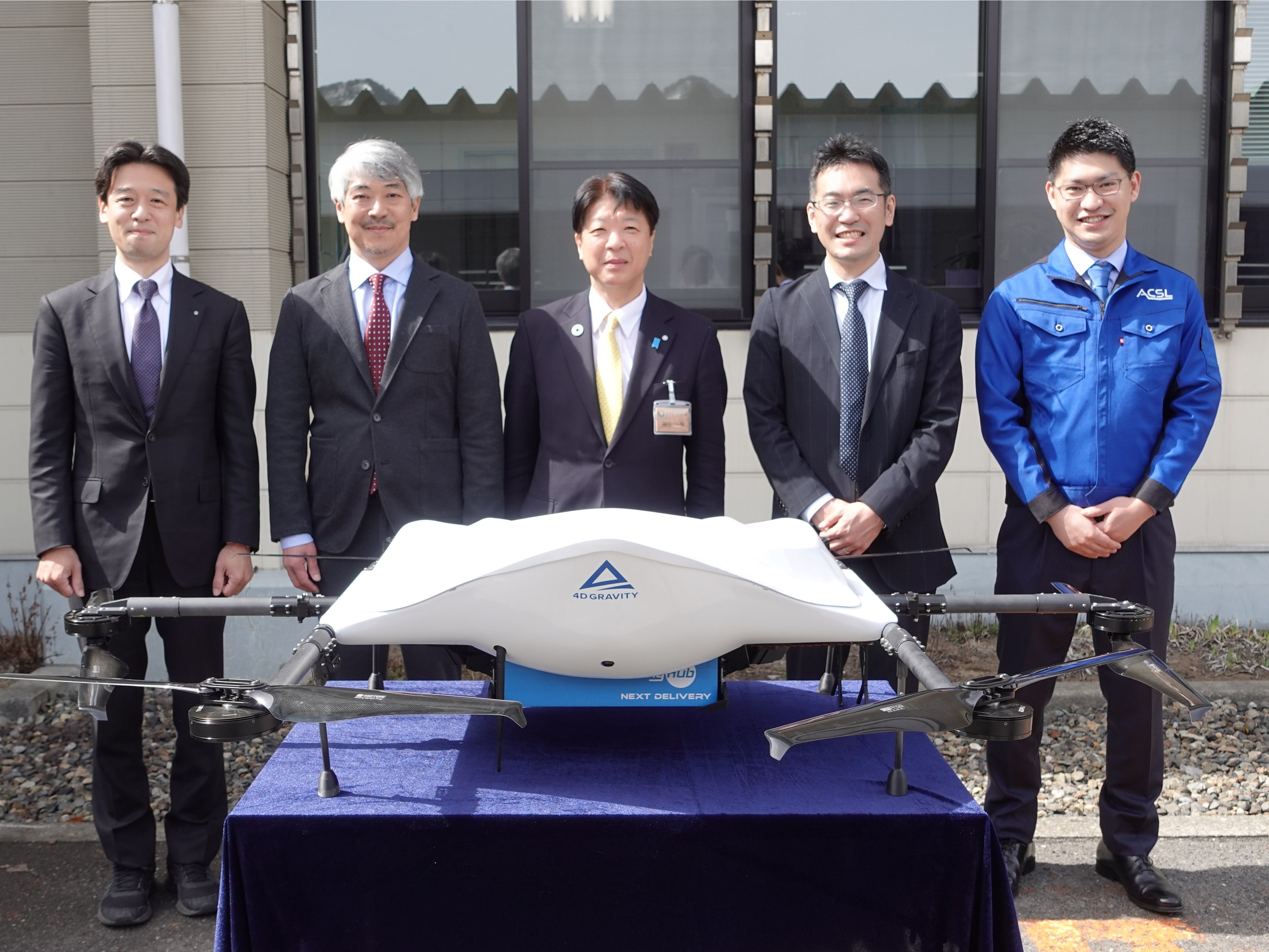 物流専用ドローンを前に写真右から、ＡＣＳＬ 代表取締役社長 兼 COO鷲谷聡之、KDDI （事業創造本部 ビジネス開発部 ドローン事業推進Ｇリーダー）博野 雅文、阿賀町長 神田一秋、エアロネクスト代表取締役CEO／NEXT DELIVERY代表取締役 田路