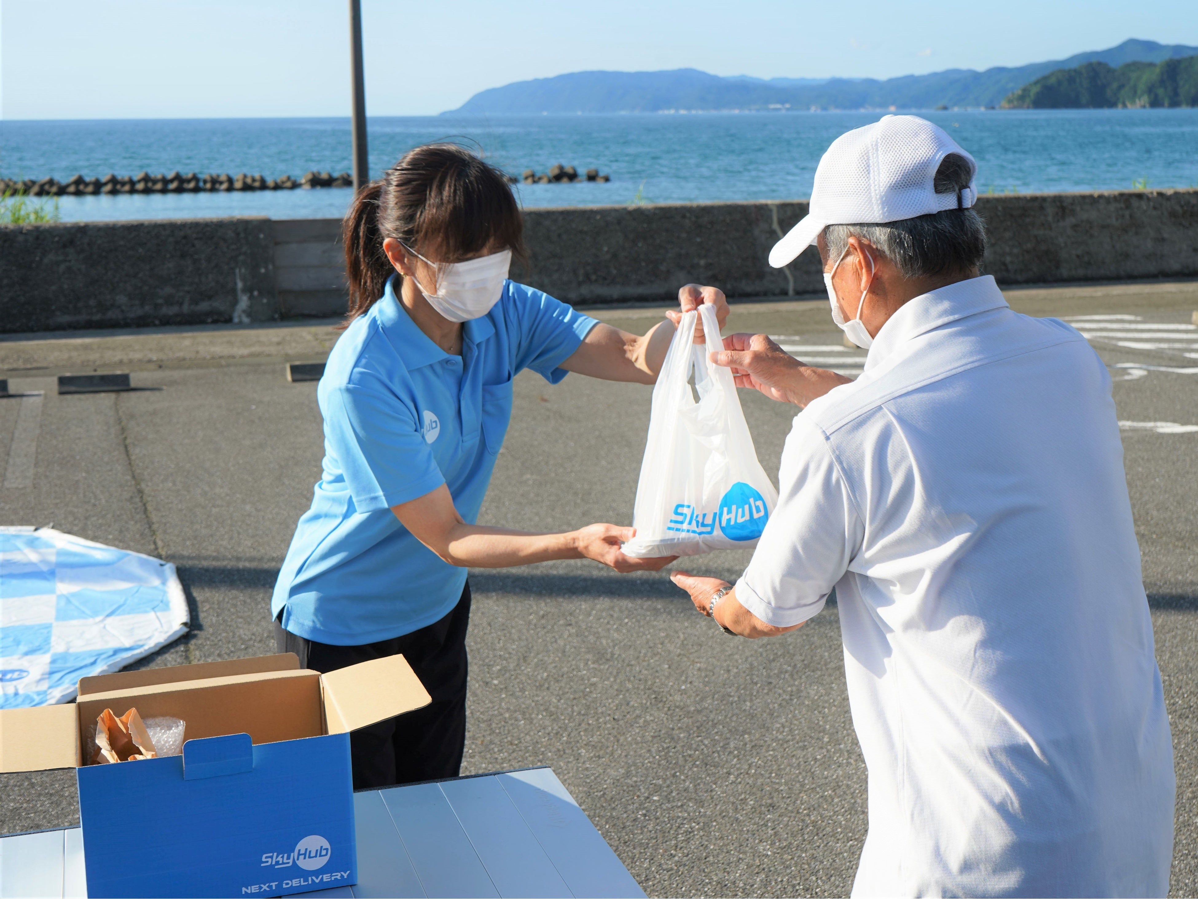 ドローン配送されたテイクアウト商品をスタッフから受取る植本太郎さん（東浦公民館前）
